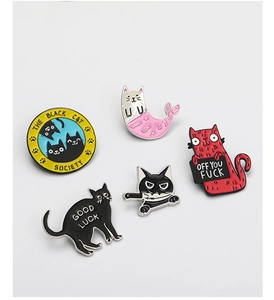 Flat lay of colorful enamel cat pins including Black Cat Society and Good Luck designs