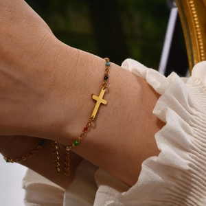 Detail of a vintage gold cross bracelet with colorful beads worn by a female model