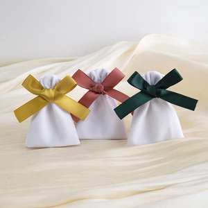 Detailed view of three white velvet drawstring bags with colorful silk ribbons