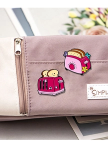 Makroaufnahme der Toaster-Emaille-Pins mit rosa Brotmotiven auf einem Federmäppchen aus Stoff
