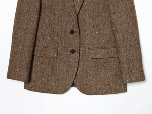 Detail of brown herringbone tweed blazer showing two-button closure and flap pockets