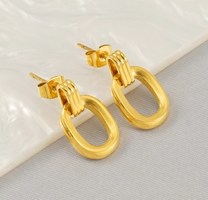 Macro shot of gold double oval link earrings on textured grey and white fabric