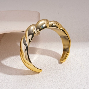 Close-up of a gold twisted cuff bracelet with a polished texture on a stone stand