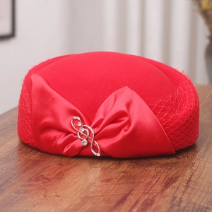 Close-up of a red wool beret featuring a large satin bow and mesh veil with a music note pin