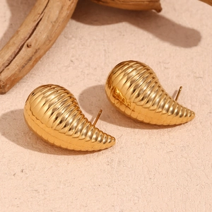 Macro shot of gold hollow spiral teardrop earrings on a textured beige sand base