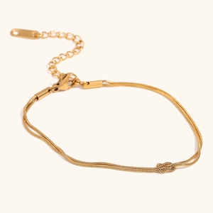 Detail of 18K gold double-layer snake chain bracelet featuring a central love knot design