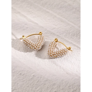 Macro shot of V-shaped 18k gold plated earrings with embedded white pearls on stone
