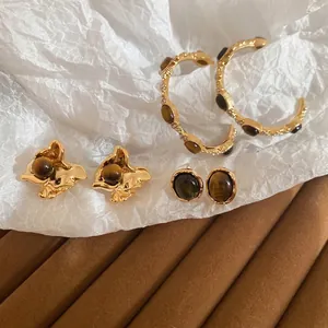 Retro gold earrings set with tiger eye stones on textured velvet and paper background