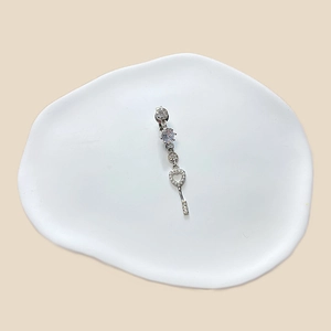 Detail shot of a silver belly ring with zircon heart and key charm on a white ceramic plate