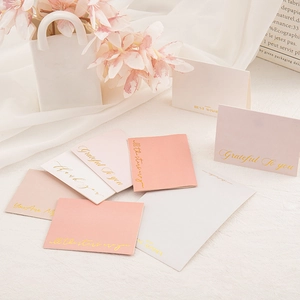 Set of pink and white greeting cards with gold foil lettering on a soft fabric background