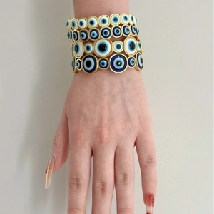 Gold-tone stacked evil eye bracelets with blue and white circular charms on a hand model