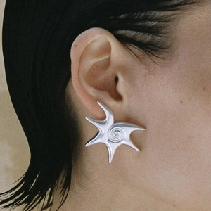 Close-up of a silver starfish earring with spiral detail worn on a model's ear