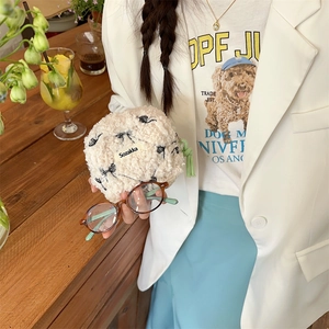 Close-up of plush floral makeup pouch with green zipper held by a model in a cafe
