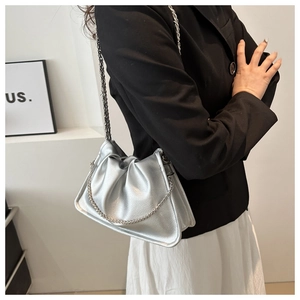 Detail view of a silver pleated baguette bag with a metallic chain strap on a black blazer