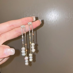 Détail de longues boucles d'oreilles dorées à pampilles avec zircons et perles