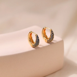 18K gold plated brass oval hoop earrings with blue zircon stones on a pink display