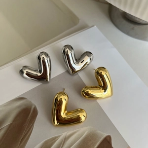 Macro detail of high-polished hollow gold and silver heart stud earrings on a book page