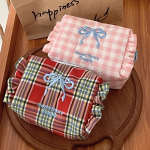 Detail view of plaid makeup bags with bow embroidery on a round wooden tray