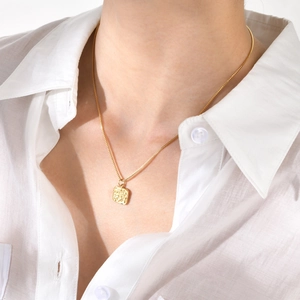 Close-up of a square embossed gold pendant on a fine chain worn by a model