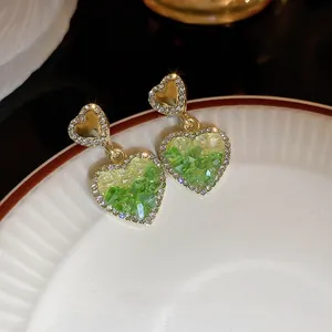 Detailed close-up of heart-shaped gold drop earrings with gradient green crystals