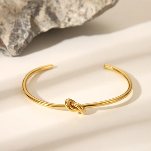 Nahaufnahme des goldenen Armreifs mit Knotendesign vor einem neutralen Hintergrund