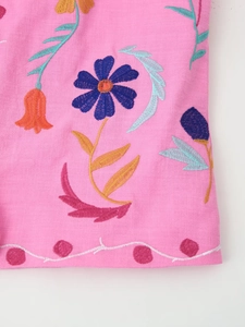 Close-up of pink linen fabric with vibrant floral embroidery and intricate wavy hem detail