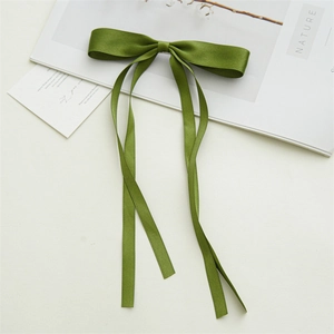 Close-up of elegant forest green satin bow hair clip with flowing ribbon on nature book