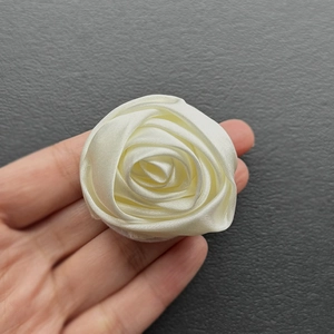 Macro view of handmade beige satin rose brooch with layered petals and silk texture