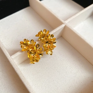 Macro detail of gold floral C-shape stud earrings nestled in a beige velvet jewelry tray