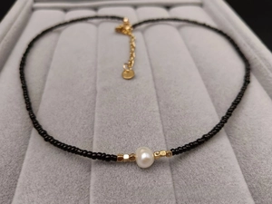 Detail of a black beaded necklace with a white baroque pearl and gold spacers on velvet