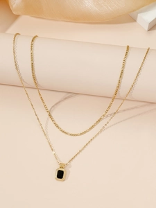 Close-up of double layer gold necklace featuring a black octagonal pendant and Figaro chain