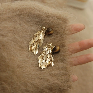 Detail of golden leaf tassel earrings featuring a round brown tiger eye stone on soft knit