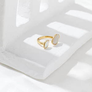 Detail of gold open ring featuring oval mother-of-pearl inlays on white geometric stand