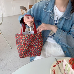 Close-up of small floral corduroy tote bag with red handles and snap button closure