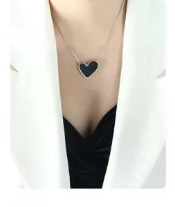 Close-up of minimalist black heart pendant necklace on model wearing a white suit