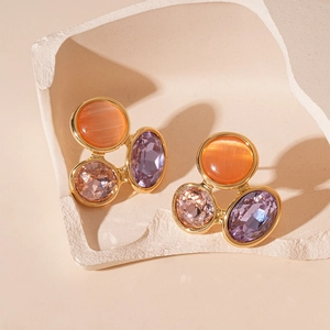 Détail de boucles d'oreilles dorées avec pierres orange et violettes sur support rocheux