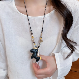 Detail of beaded necklace featuring a black leather horse pendant with golden lucky bag charm