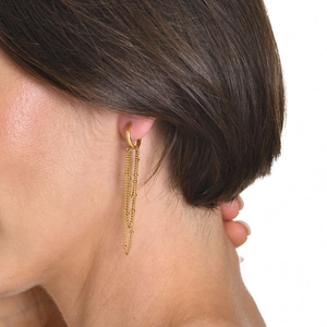 Detail view of golden multi-layer beaded chain tassel earrings worn by a model