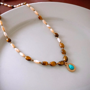 Detailed shot of tiger eye beads and turquoise teardrop pendant in golden metal setting