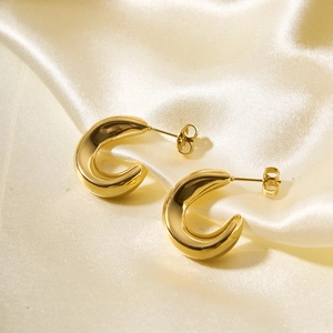 Close-up of chunky gold C-shaped hoop earrings on elegant beige satin fabric