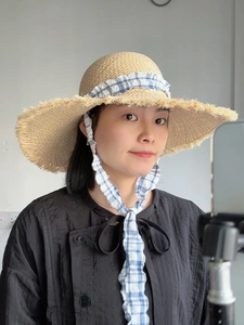 Detailed close-up of a raffia sun hat with frayed edges and blue checkered ribbon tie