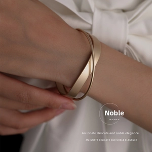Close-up of minimalist matte gold geometric crisscross bangle on woman's wrist