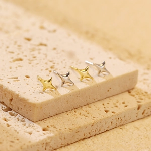 Macro shot of minimalist gold and silver four-point star studs on a stone display
