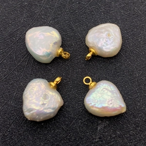 Macro view of four white baroque heart pearl pendants with golden rings on black texture
