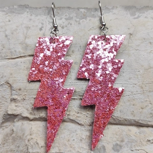 Dettaglio degli orecchini a saetta con glitter rosa su una superficie marmorizzata