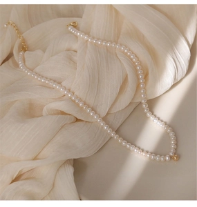 Detail of a natural pearl necklace with gold ball clasp on soft beige pleated fabric