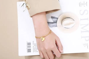 Elegant gold heart charm bangle bracelet shown on model with lifestyle magazine background