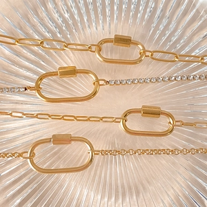 Quattro bracciali moschettone in acciaio dorato con strass presentati su un piatto di vetro