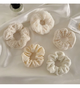 Set of five cream-colored plush and velvet hair scrunchies on white silk fabric