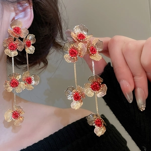 Detail of elegant gold metal flower tassel earrings with red roses on female model